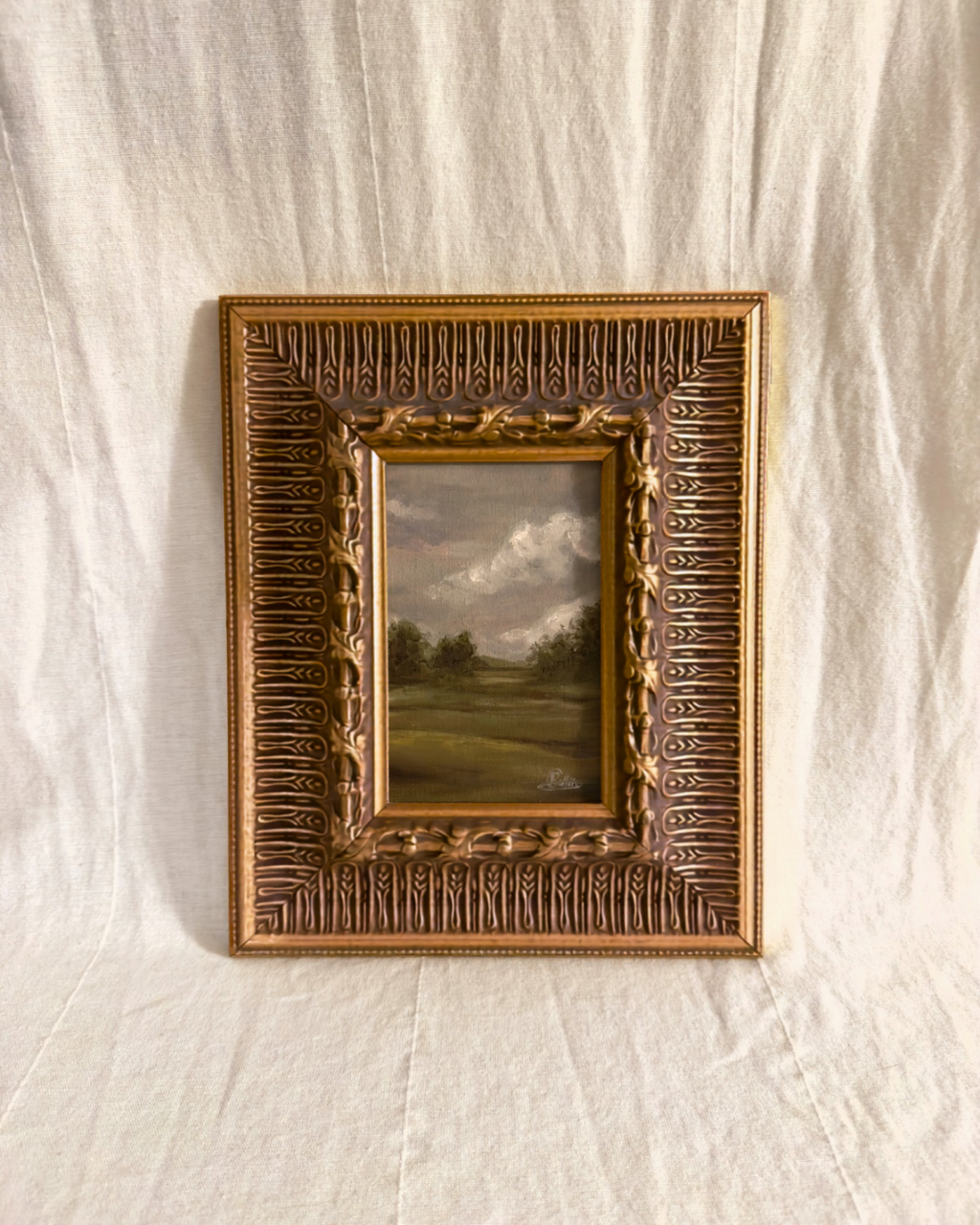 Wide ornate antique gilt frame with a grey small moody british countryside landscape painting inside photographed on a textured white background