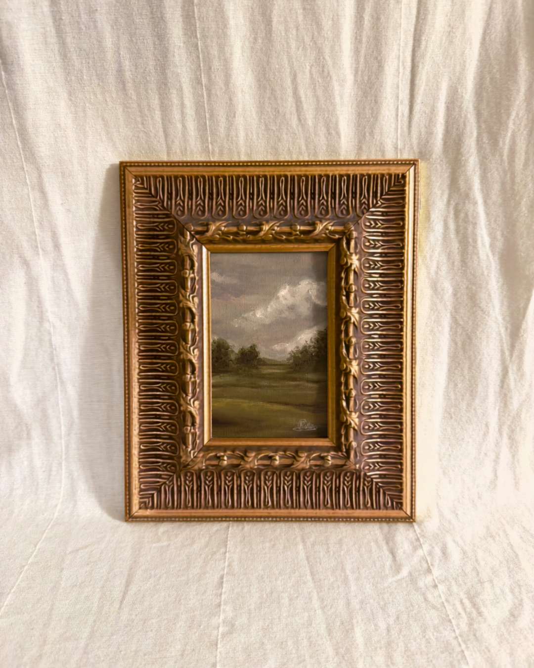 Wide ornate antique gilt frame with a grey small moody british countryside landscape painting inside photographed on a textured white background